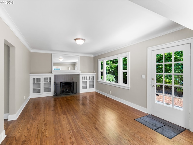 unfurnished living room featuring a tiled fireplace, crown molding, and wood-type flooring