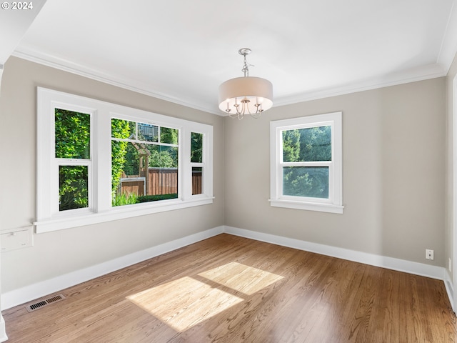 spare room featuring hardwood / wood-style floors, crown molding, a notable chandelier, and a healthy amount of sunlight