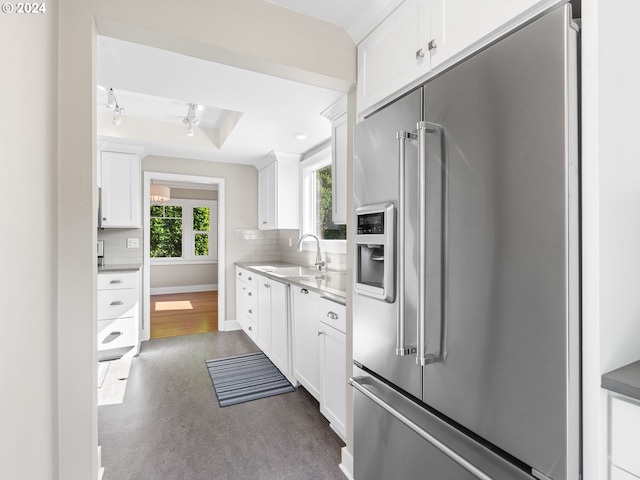 kitchen with high quality fridge, white cabinets, decorative backsplash, sink, and a tray ceiling