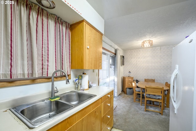 kitchen featuring white refrigerator with ice dispenser, sink, light carpet, and a textured ceiling