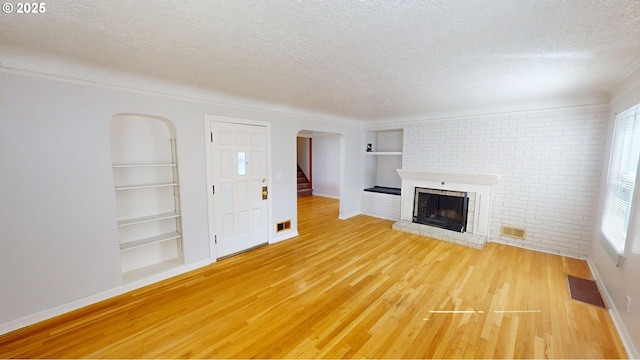 unfurnished living room with hardwood / wood-style floors, a textured ceiling, built in features, and a brick fireplace