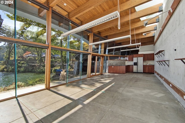 interior space with concrete floors, a towering ceiling, a healthy amount of sunlight, and a water view