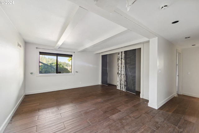 empty room with baseboards, visible vents, wood finished floors, and beam ceiling