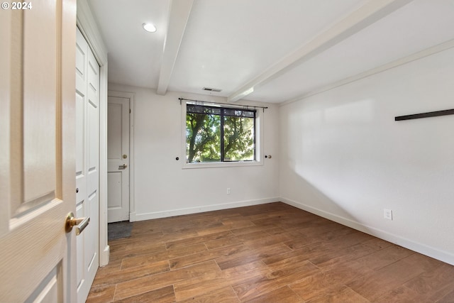 empty room featuring beamed ceiling, visible vents, wood finished floors, and baseboards