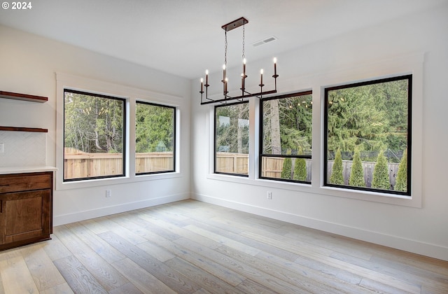 unfurnished dining area featuring light wood-type flooring and an inviting chandelier