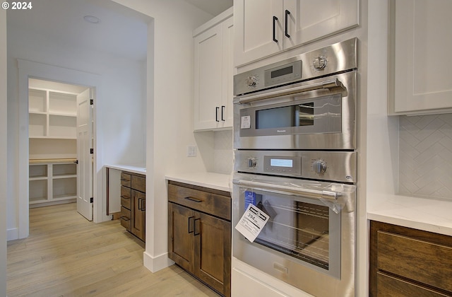 kitchen with white cabinets, backsplash, light hardwood / wood-style floors, and double oven