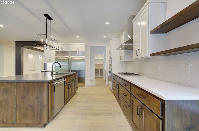 kitchen with appliances with stainless steel finishes, a kitchen island with sink, decorative light fixtures, light hardwood / wood-style flooring, and white cabinets