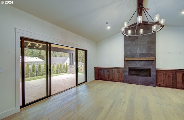 unfurnished living room featuring a tile fireplace, light wood-type flooring, an inviting chandelier, and vaulted ceiling