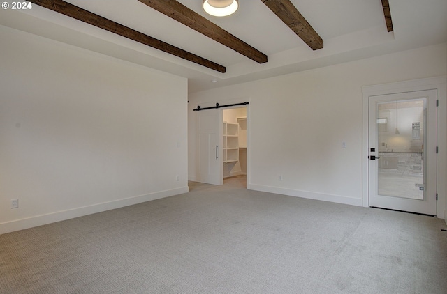 unfurnished room with a barn door, beam ceiling, and light carpet