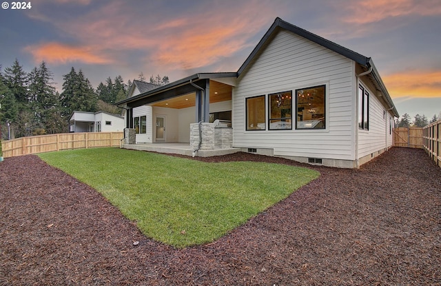 back house at dusk featuring a patio area and a yard