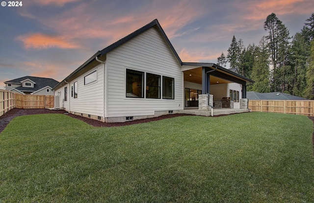 back house at dusk featuring a lawn and a patio area