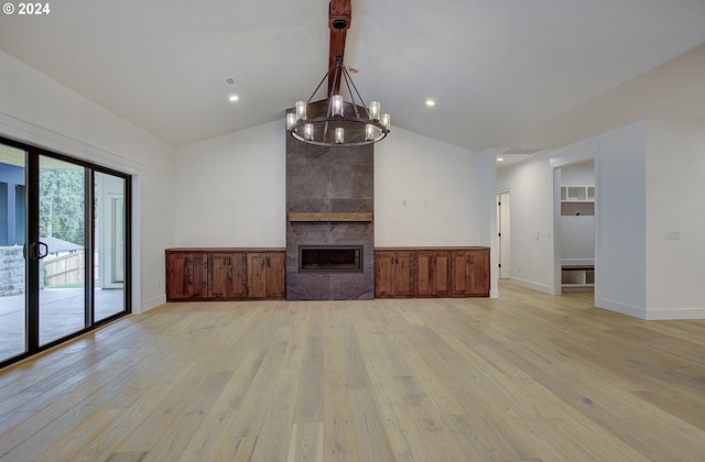 unfurnished living room featuring a tiled fireplace, light hardwood / wood-style flooring, lofted ceiling, and a notable chandelier