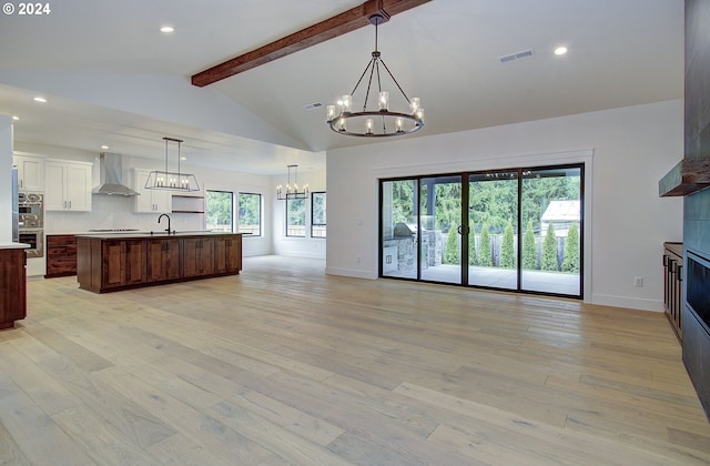 kitchen featuring a wealth of natural light, a center island with sink, wall chimney exhaust hood, and light wood-type flooring