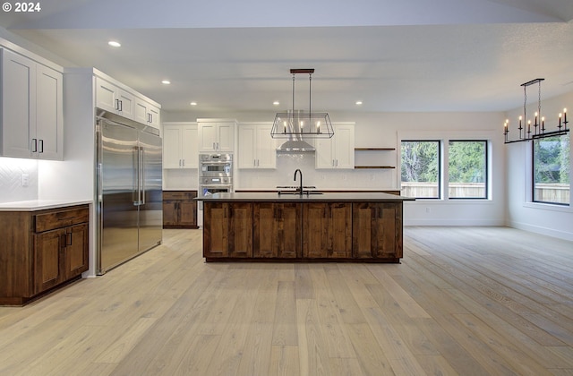 kitchen with stainless steel appliances, hanging light fixtures, a center island with sink, and light hardwood / wood-style floors