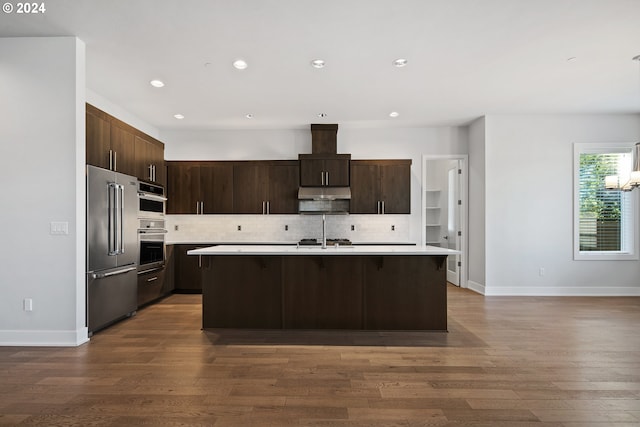 kitchen with wood-type flooring, a kitchen island with sink, stainless steel appliances, and dark brown cabinetry