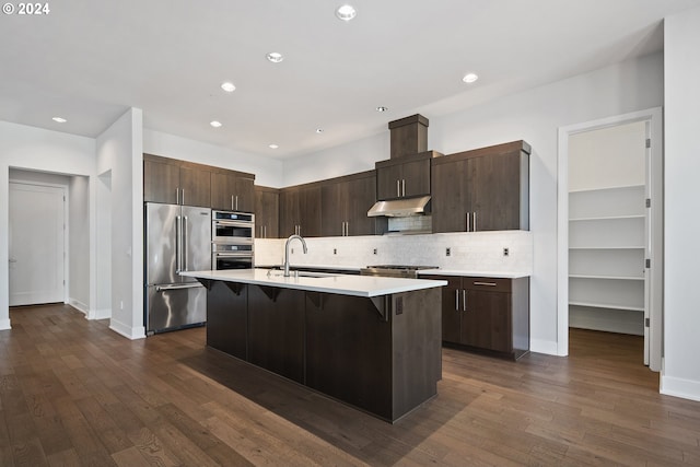 kitchen with a breakfast bar area, sink, dark hardwood / wood-style floors, appliances with stainless steel finishes, and an island with sink