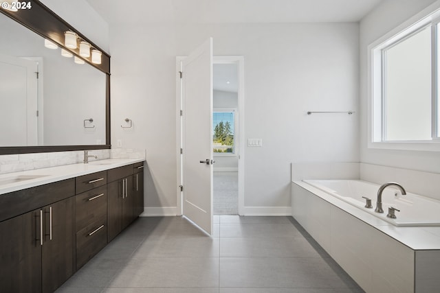 bathroom with tile patterned flooring, a relaxing tiled tub, vanity, and a healthy amount of sunlight