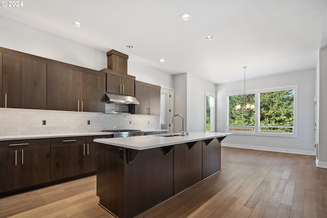 kitchen featuring pendant lighting, a center island with sink, a breakfast bar area, light hardwood / wood-style floors, and decorative backsplash