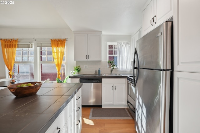 kitchen with stainless steel appliances, white cabinetry, tile counters, and decorative backsplash