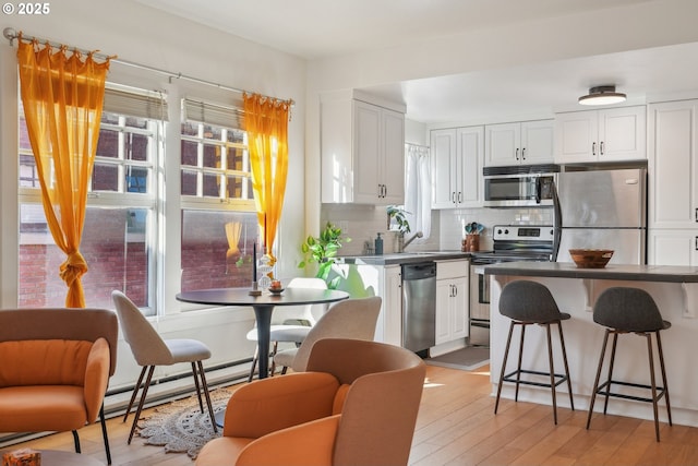 kitchen featuring appliances with stainless steel finishes, tasteful backsplash, a baseboard radiator, white cabinets, and light wood-type flooring