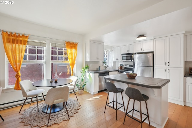 kitchen with white cabinets, a kitchen breakfast bar, appliances with stainless steel finishes, and light wood-type flooring