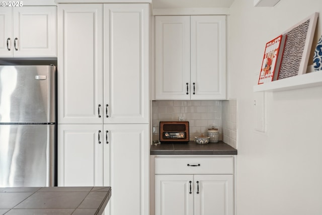 kitchen with white cabinets, stainless steel fridge, and tasteful backsplash