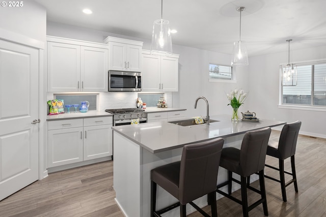 kitchen with stainless steel appliances, sink, white cabinets, hanging light fixtures, and an island with sink