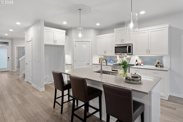 kitchen with hanging light fixtures, a center island with sink, white cabinets, and stainless steel appliances