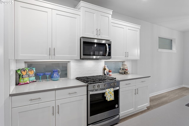 kitchen with tasteful backsplash, white cabinetry, light wood-type flooring, and appliances with stainless steel finishes