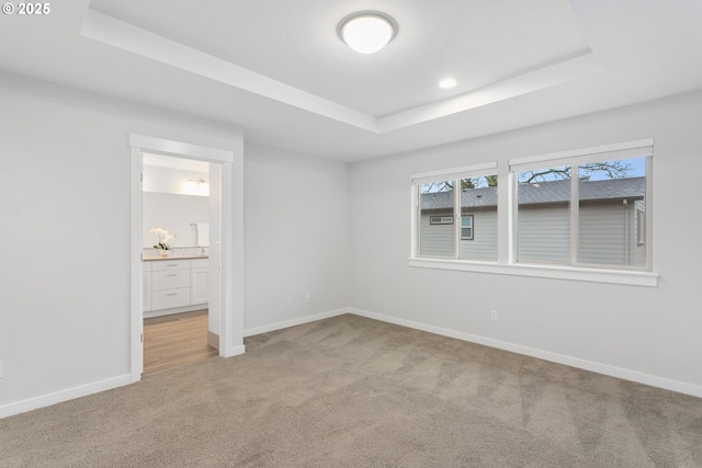 unfurnished bedroom featuring connected bathroom, a tray ceiling, and light colored carpet