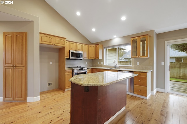 kitchen with light stone countertops, appliances with stainless steel finishes, sink, a center island, and light hardwood / wood-style floors