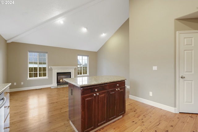 kitchen featuring light wood-type flooring, lofted ceiling with beams, a center island, and light stone counters