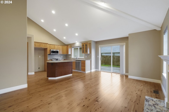 kitchen featuring stainless steel appliances, beamed ceiling, backsplash, a kitchen island, and light wood-type flooring