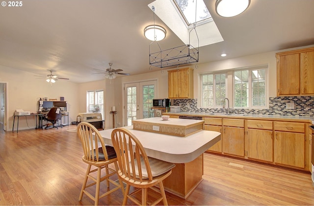 kitchen with sink, a kitchen island, a skylight, and light wood-type flooring