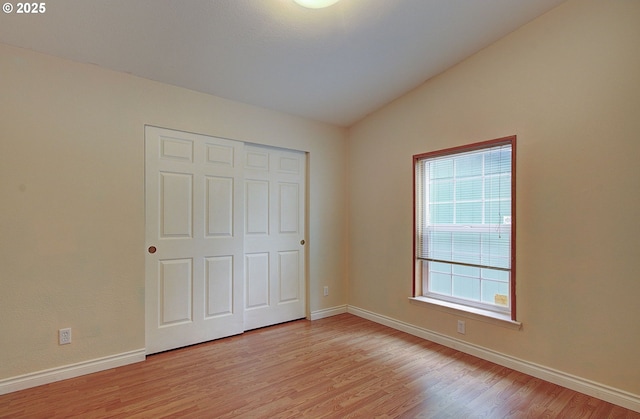 unfurnished bedroom featuring light hardwood / wood-style floors, a closet, and lofted ceiling