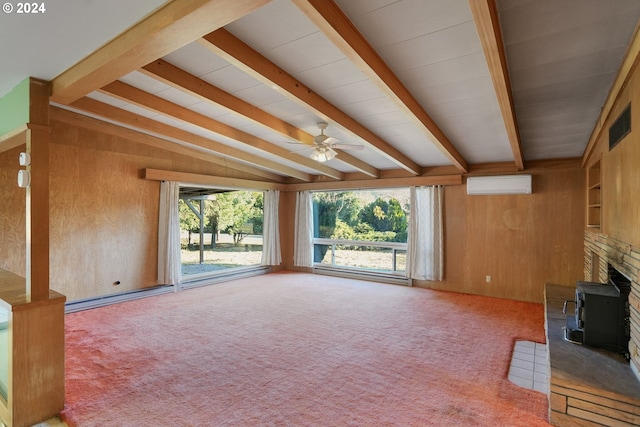 unfurnished living room featuring a wood stove, ceiling fan, a wall mounted AC, carpet floors, and wooden walls