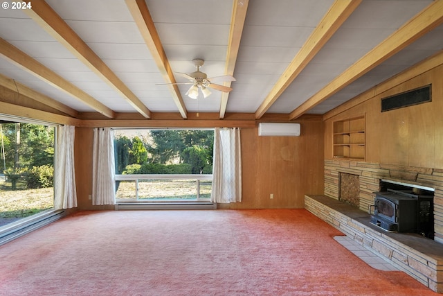 unfurnished living room with carpet flooring, ceiling fan, wooden walls, beamed ceiling, and a wood stove