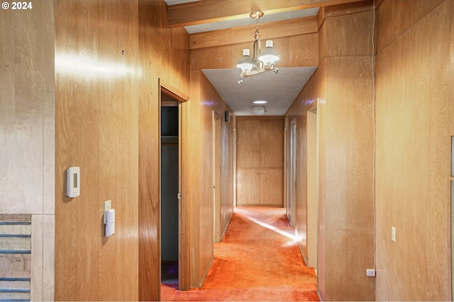 hall with wood walls, high vaulted ceiling, beamed ceiling, a notable chandelier, and carpet floors