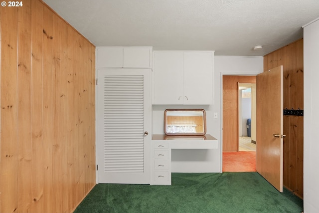 kitchen featuring carpet, wood walls, white cabinetry, and a textured ceiling