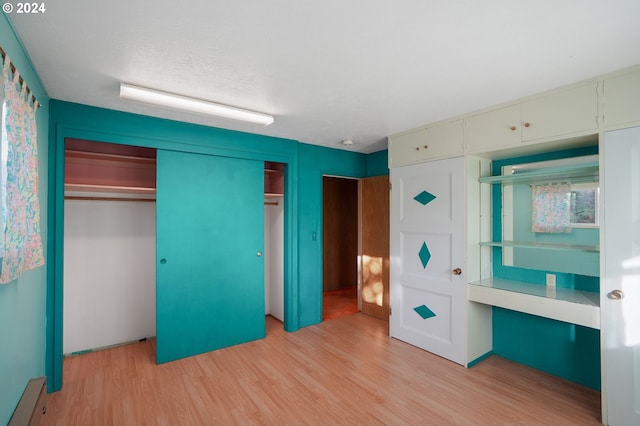 unfurnished bedroom featuring light wood-type flooring, a closet, and baseboard heating