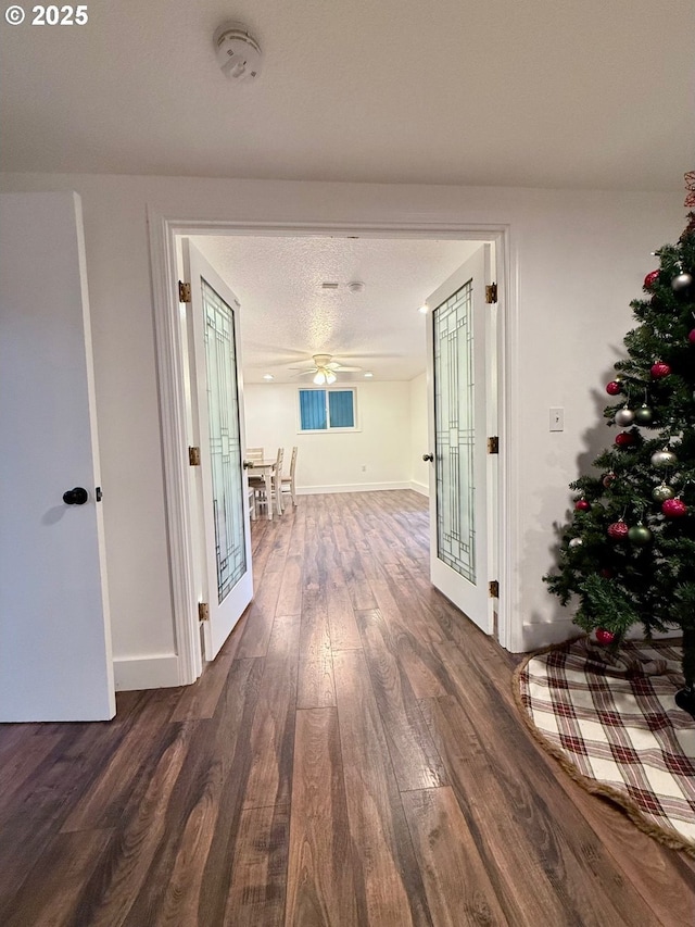 hallway with dark wood-type flooring, a textured ceiling, and french doors