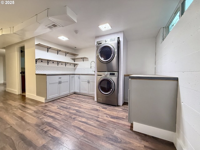 clothes washing area with dark wood-type flooring, stacked washer and clothes dryer, and cabinets