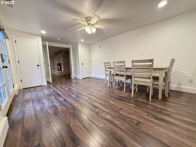 dining room featuring ceiling fan, a brick fireplace, and dark hardwood / wood-style flooring