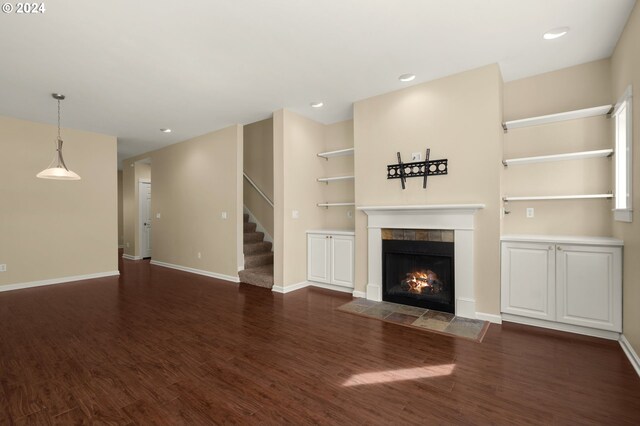 unfurnished living room with built in shelves, dark wood-type flooring, and a tile fireplace