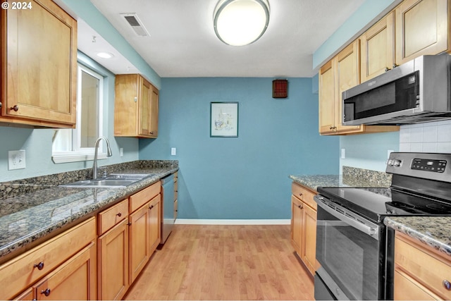 kitchen featuring appliances with stainless steel finishes, tasteful backsplash, dark stone counters, sink, and light hardwood / wood-style flooring