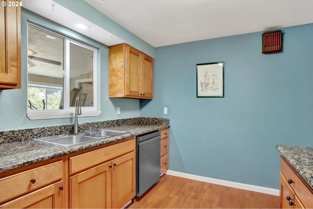 kitchen featuring stainless steel dishwasher, dark stone countertops, light wood-type flooring, and sink