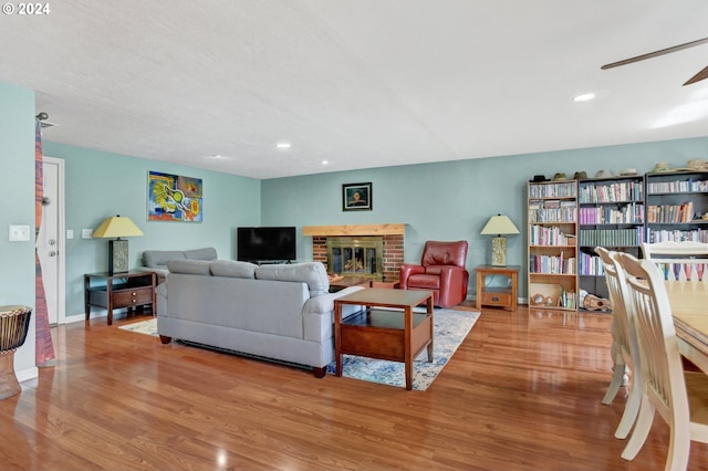 living room with ceiling fan, light hardwood / wood-style floors, and a brick fireplace