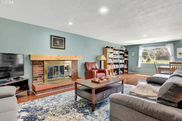 living room with ceiling fan, hardwood / wood-style floors, a textured ceiling, and a brick fireplace