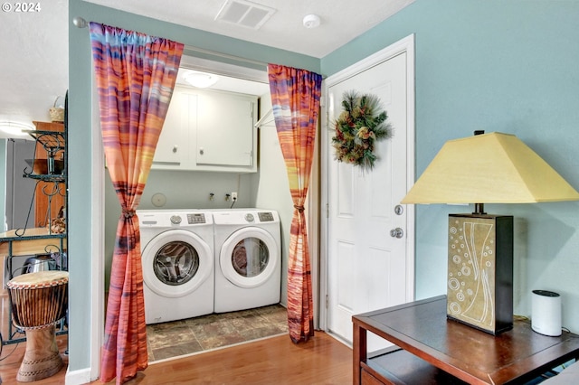 clothes washing area with washer and dryer, cabinets, and hardwood / wood-style flooring