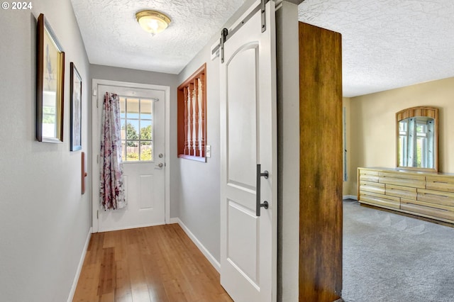 hallway featuring a barn door, a textured ceiling, and light wood-type flooring